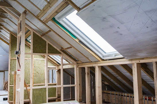 Chantier de rénovation de combles avec charpente bois apparente, isolation en laine minérale verte entre chevrons