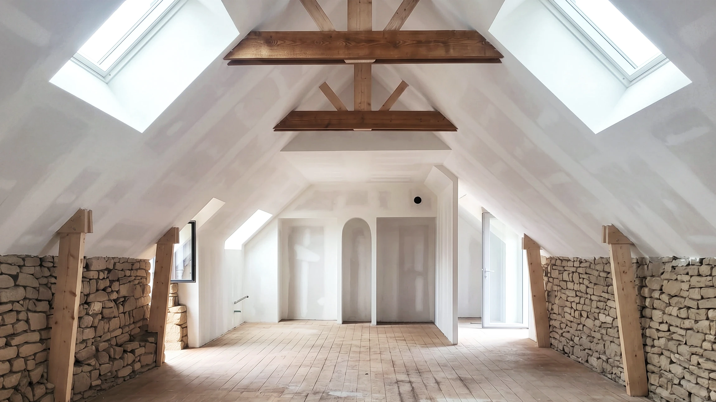 Grenier en cours de rénovation, vaste espace sous combles avec plancher en bois brut, mur en pierre apparente, cloisons en placo joints non finis